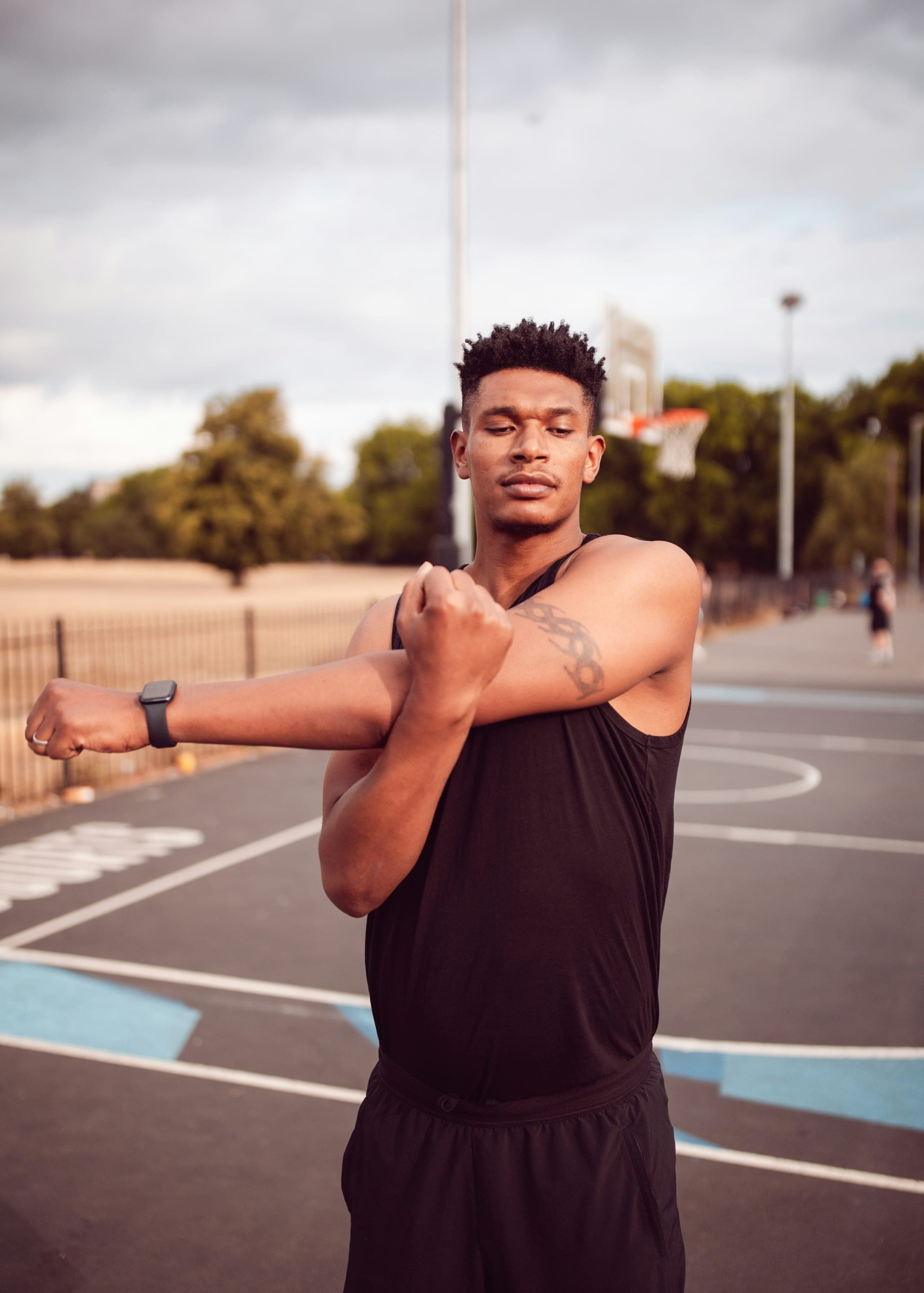 An athletic man stretching his shoulder on an outdoor court